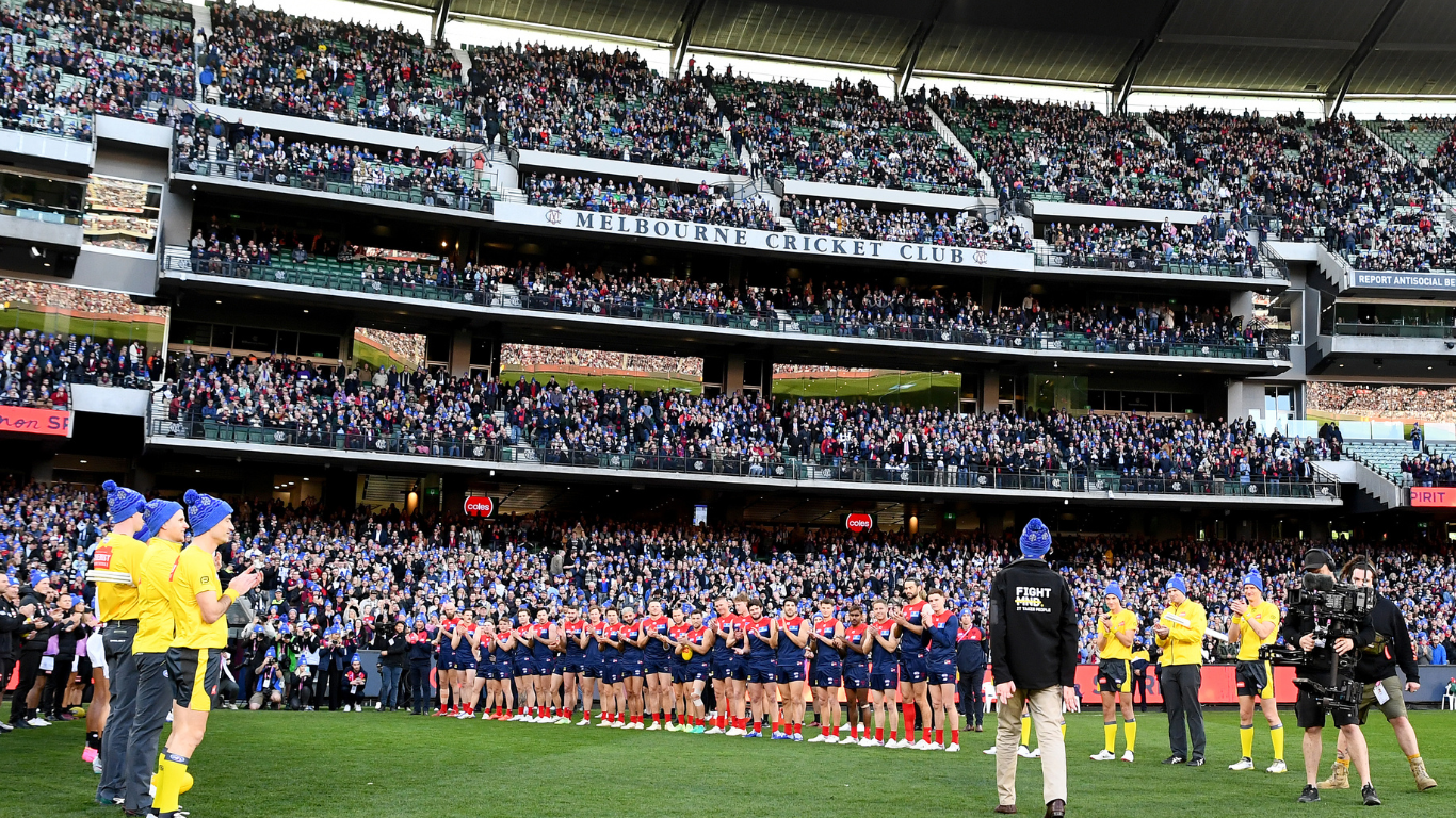 Fans at the MCG cheering during the King’s Birthday AFL Match 2025 with Big Freeze 11 banners in the background